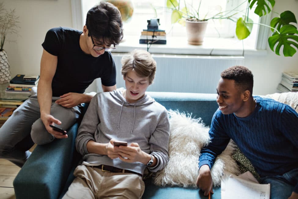 High angle view of social media addicted friends using smart phones on sofa during homework in living room