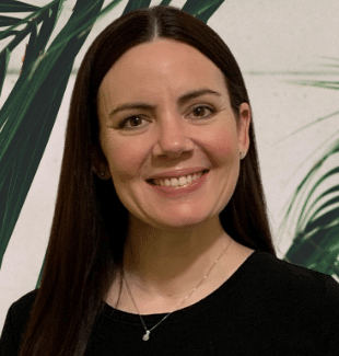 a woman smiling in front of plants.