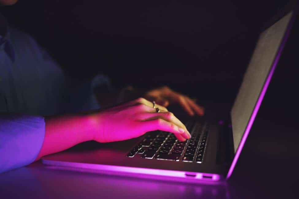 Woman sitting in the dark using backlit keyboard to type on laptop computer, implying focus and determination to keep working into the night.
